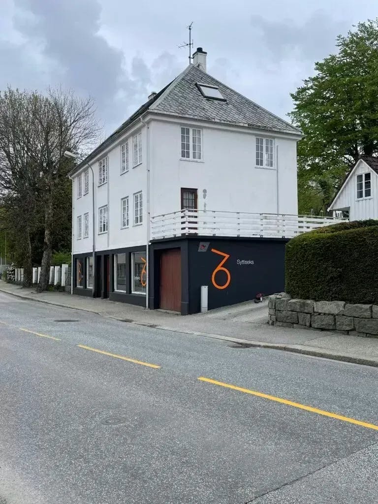 Strandgata 76 sett fra veien fra Stavanger mot Sandnes. Bygningen har en svart garasje med logoen til Syttiseks på siden